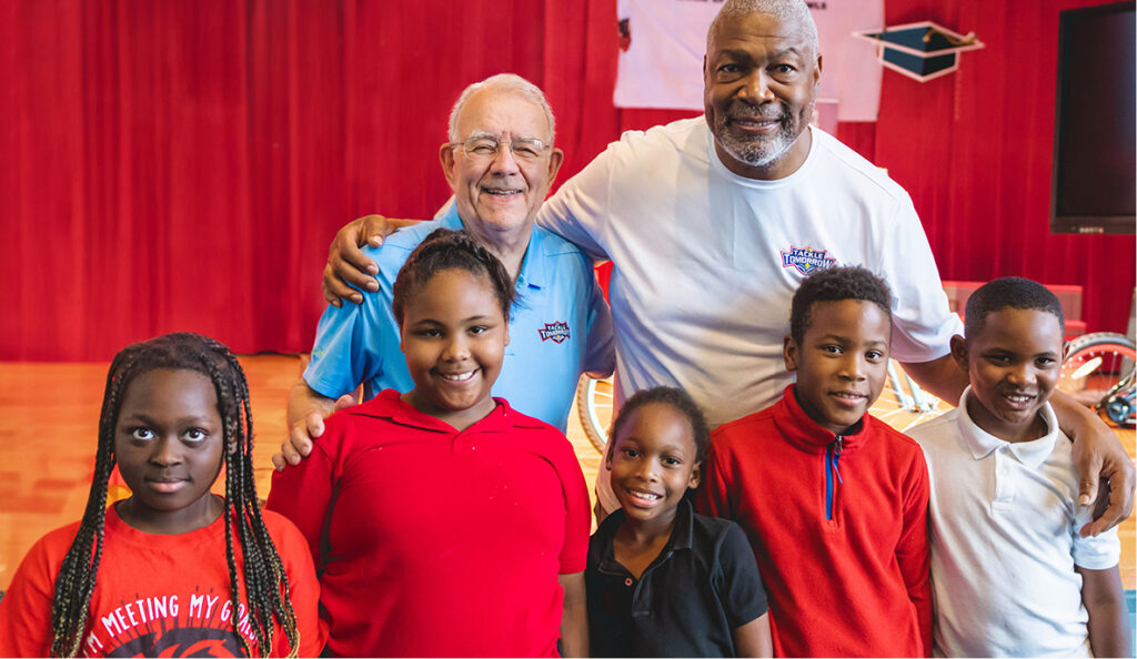 Tackle Tomorrow volunteers with students in front of a red backdrop